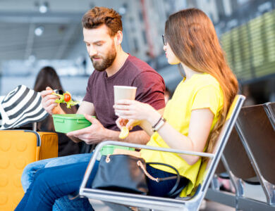 Young couple having a snack with lunch boxes at the waiting hall of the airport during their vacation