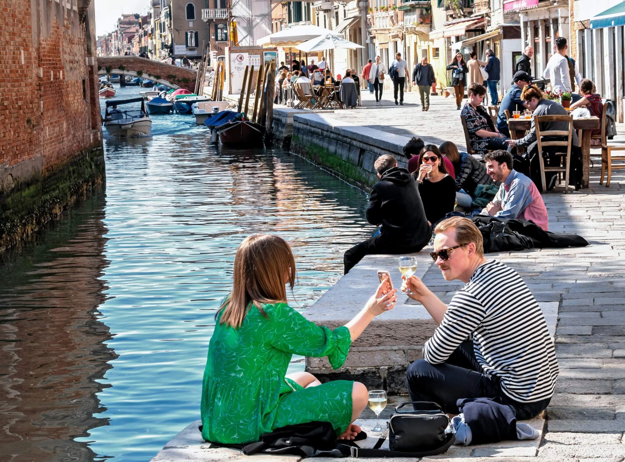 young couple sitting on side of canal toasting each other