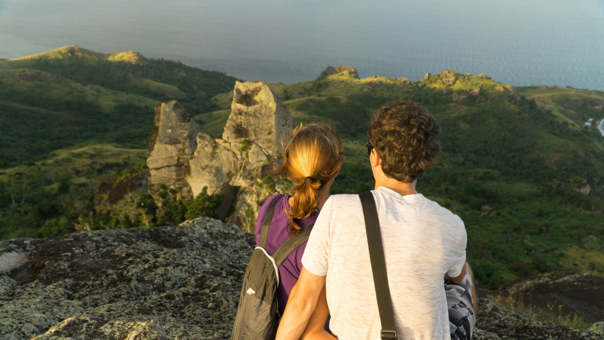 Young couple sitting on the top of the hill during golden sunset, Fiji.