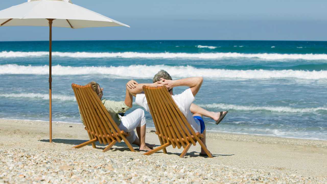 two people sit in chairs on the beach under an umbrella