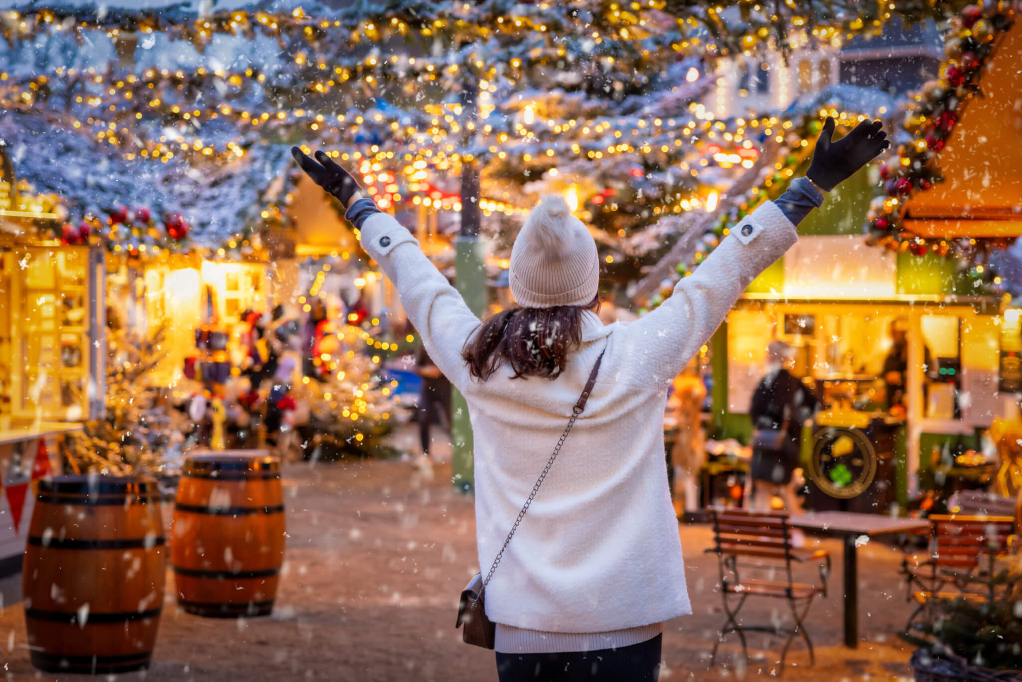 A happy tourist woman stands on a christmas market in Copenhagen, Denmark, with snow and illuminated decorations during winter time