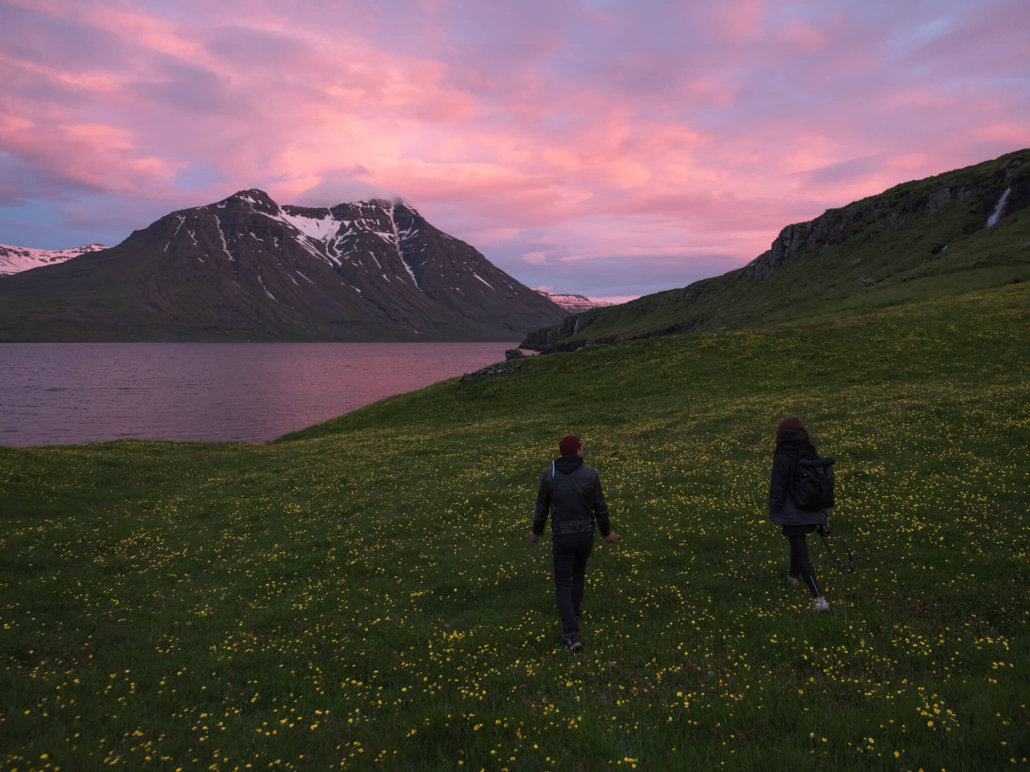 Couple walking on grassy hill near fjord in evening