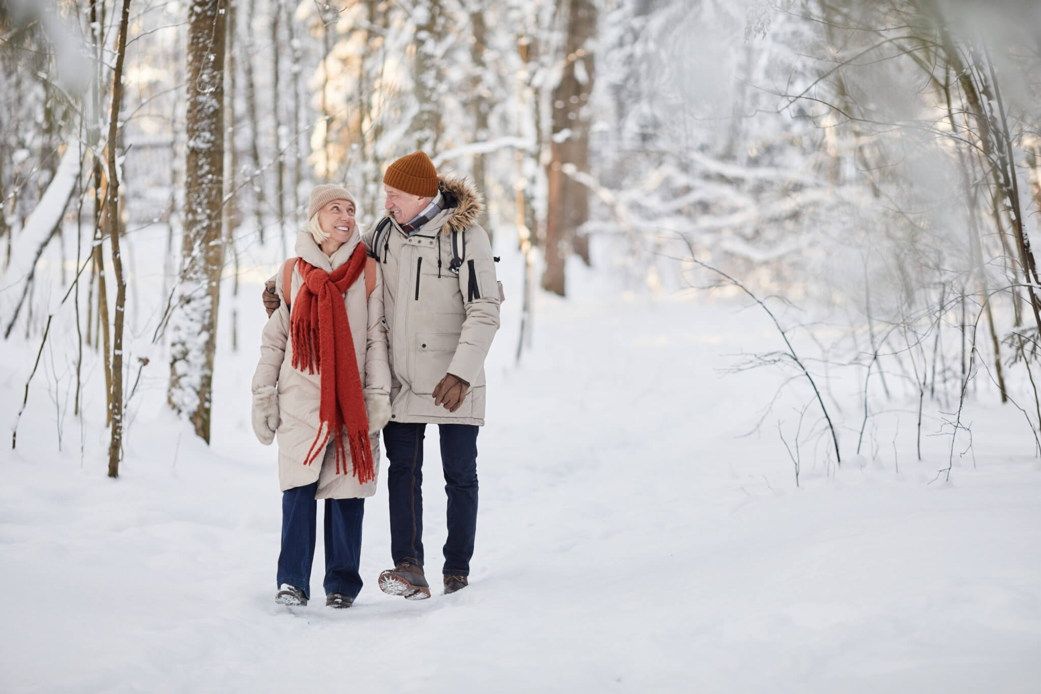 Full length portrait of happy senior couple enjoying walk in winter forest and looking at each other, copy space