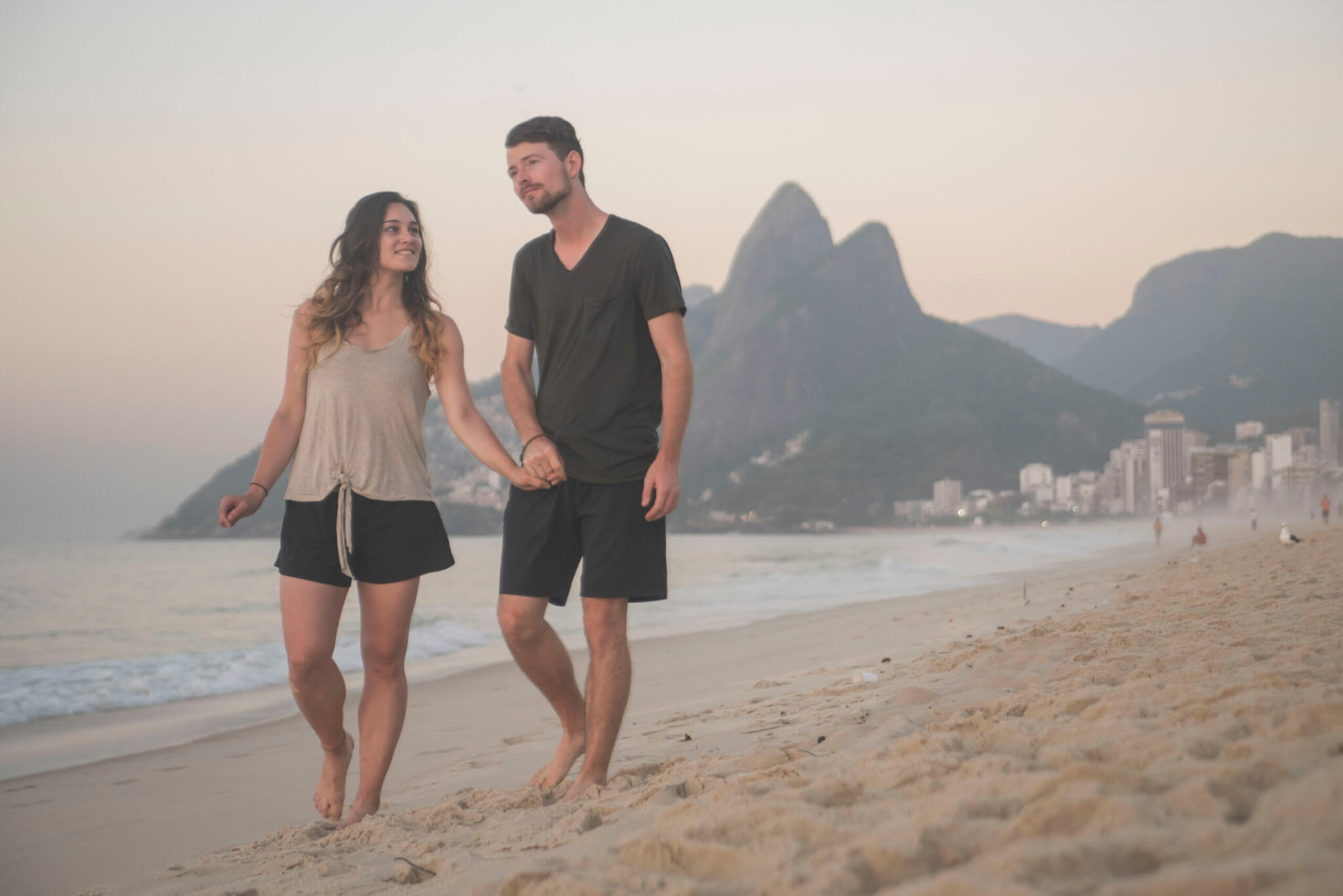 happy travel couple walking along beach in rio de janeiro brazil