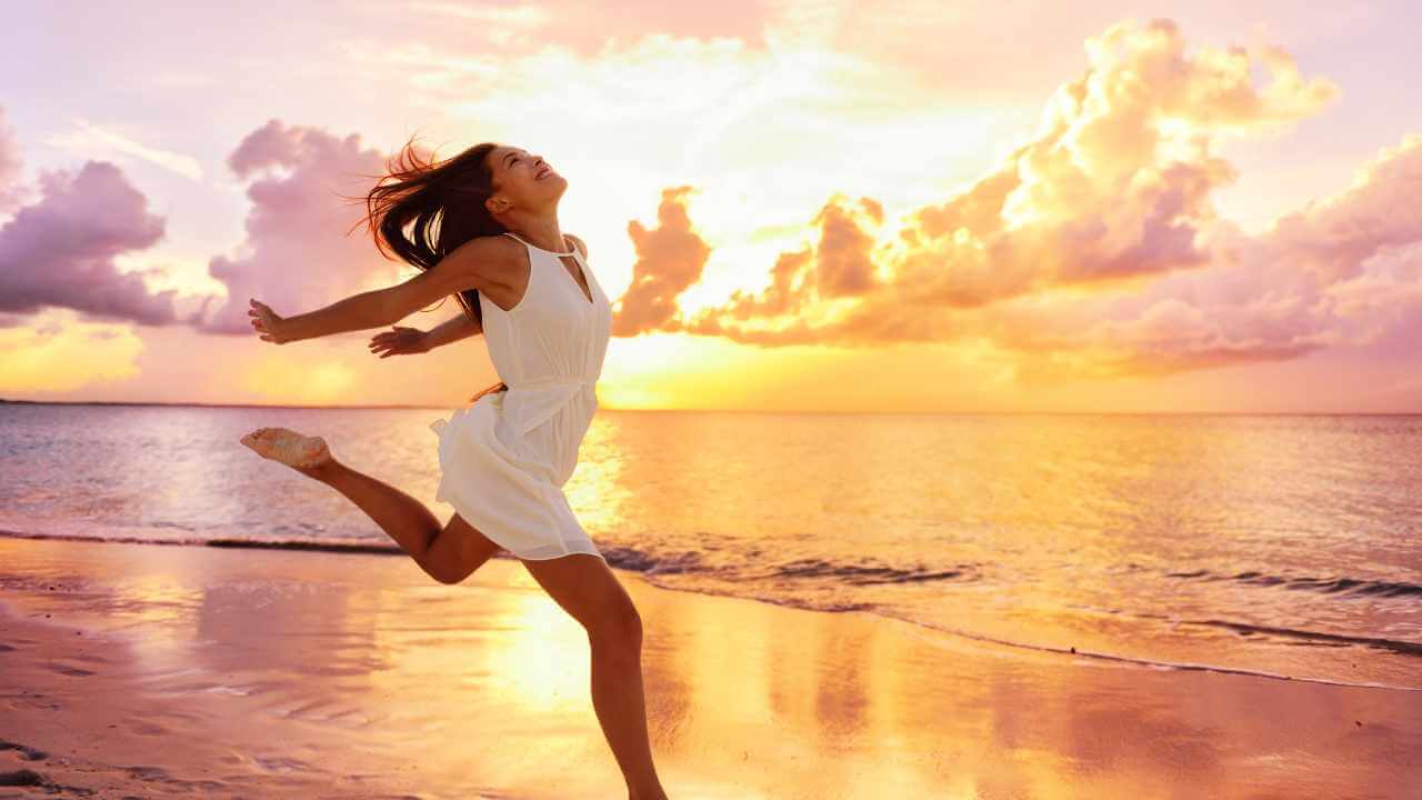 a person in a white dress is jumping on the beach at sunset