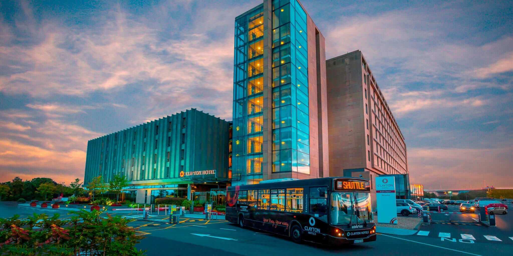 The outside of the Clayton Hotel with views of a beautiful sunset, along with the airport shuttle the hotel has to offer