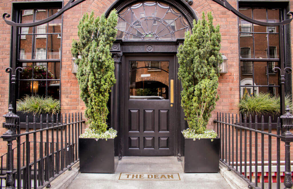 The Dean Hotel - Brown front door lines with plants with a red brick exterior 