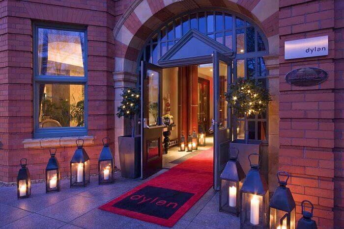 The front door of the Dylan hotel lit up at night, candles lighting the walkway with a red carpet