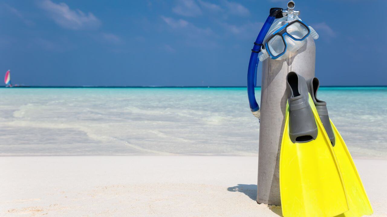 scuba diving equipment on the sand in front of the crystal blue ocean 