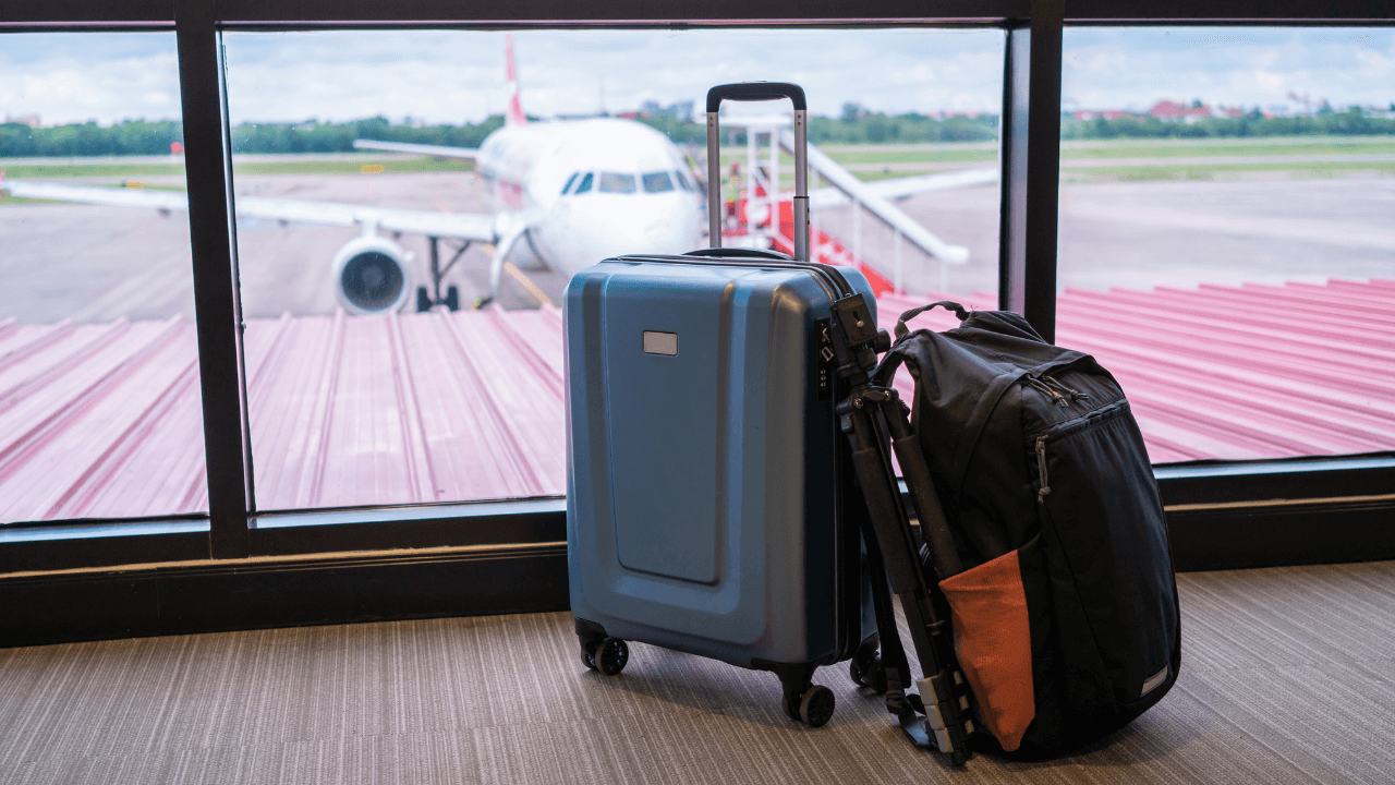 a backpack and carry on suitcase in front of a window with the plane in the background 