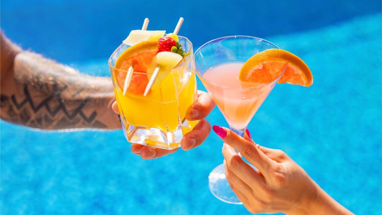 man and woman clinking their fruity drinks together with pool water in the background