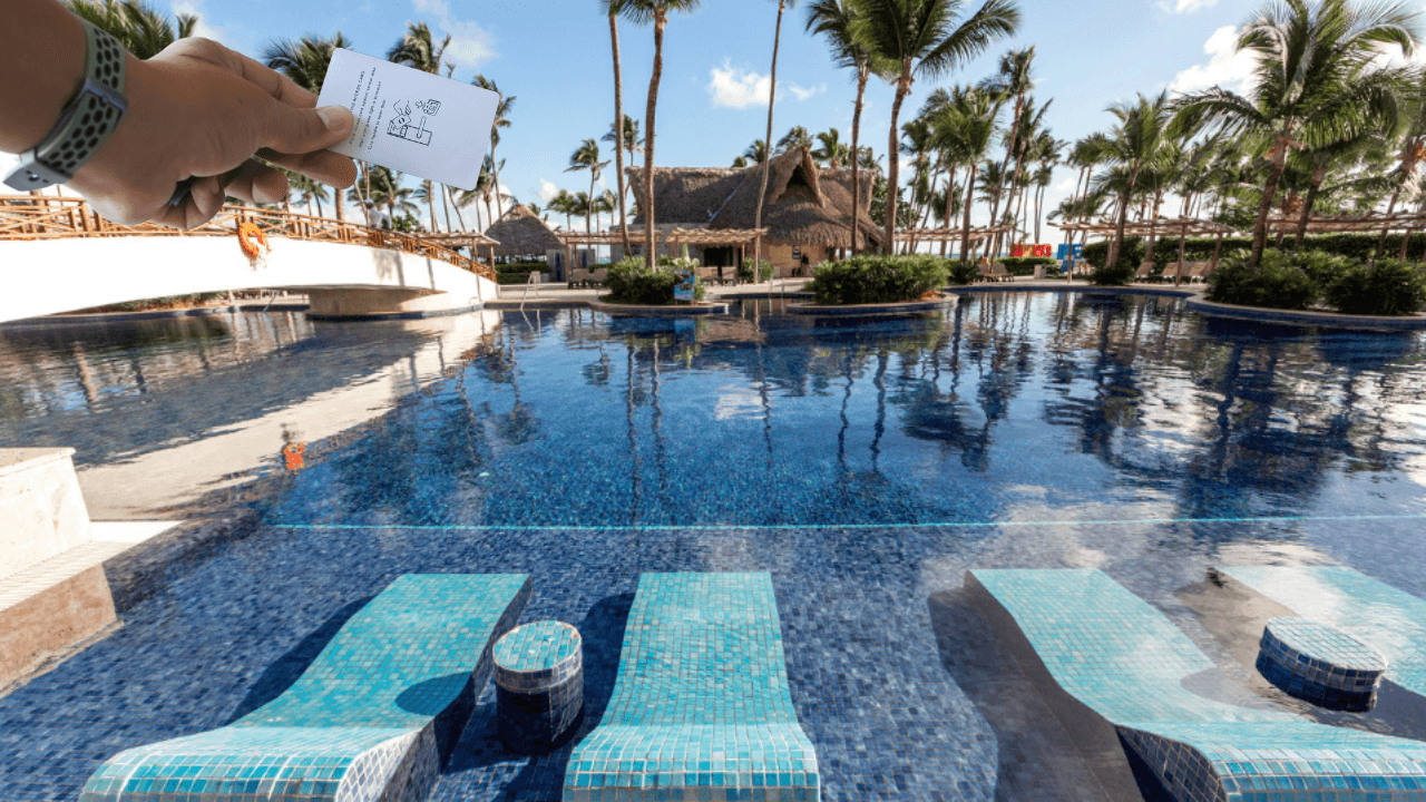 the luxury resort pool in punta cana  with a hand showing off the resort credit they get when booking this resort  package through costco travel 