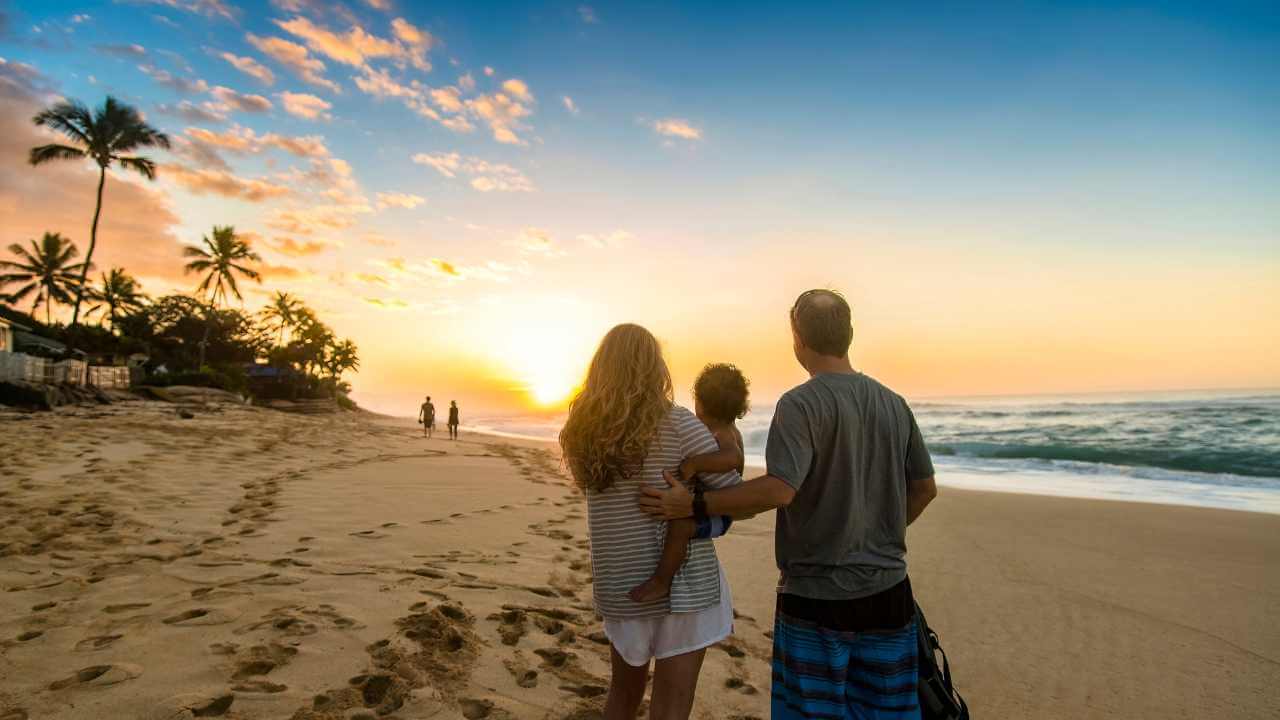 mom, dad and son facing the sunset on the beach in hawaii