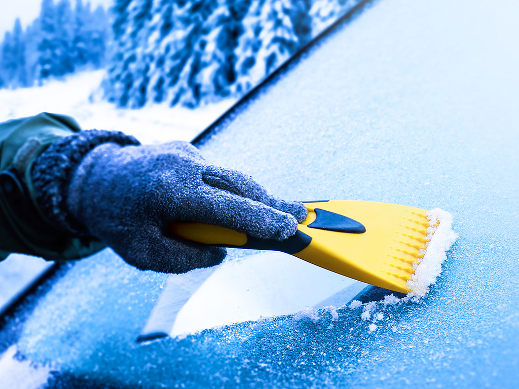 A hand using a tool to scrape ice off a car's windshield