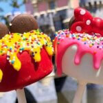 red and white cake pops with mickey and minnie ears on top in front of disney castle