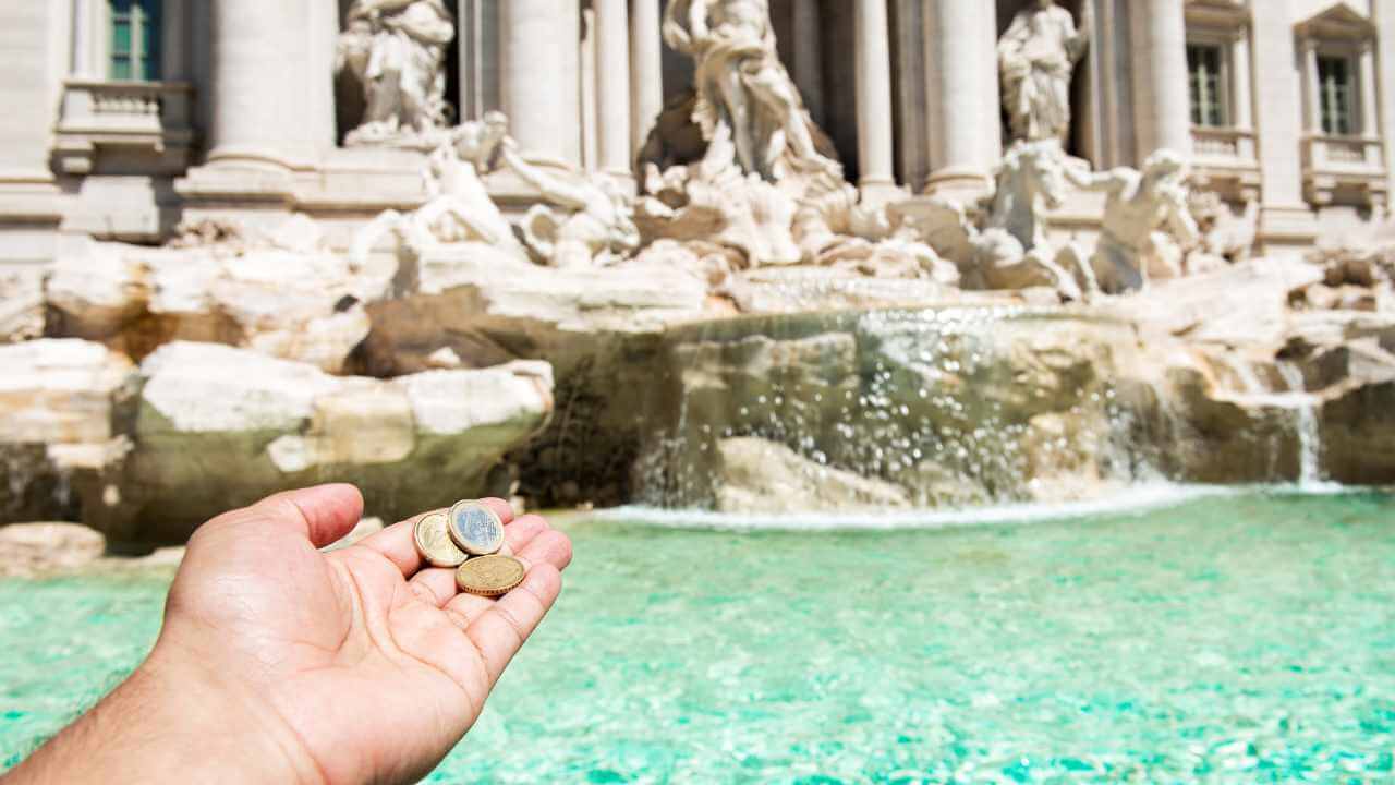 person holding coins in front of trevi fountain