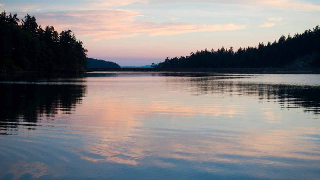 a lake surrounded by pine trees at sunset