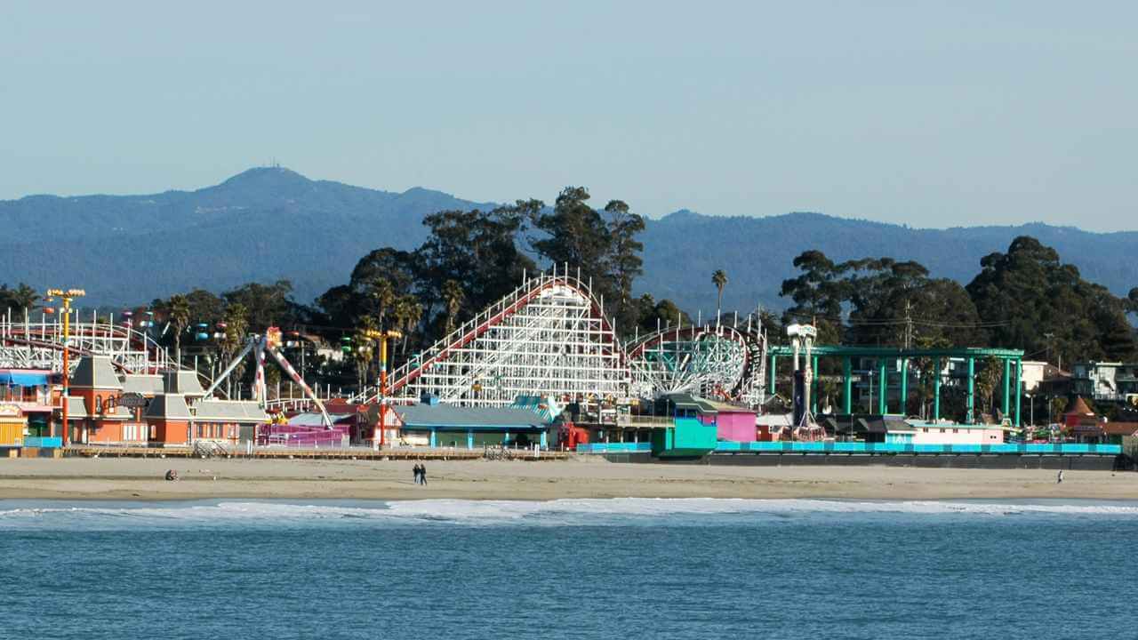 a beach with amusement rides and mountains in the background
