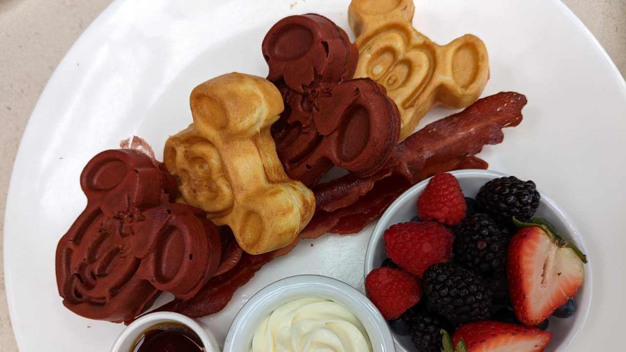 mickey waffles on a plate with fruit and whipped cream on the side