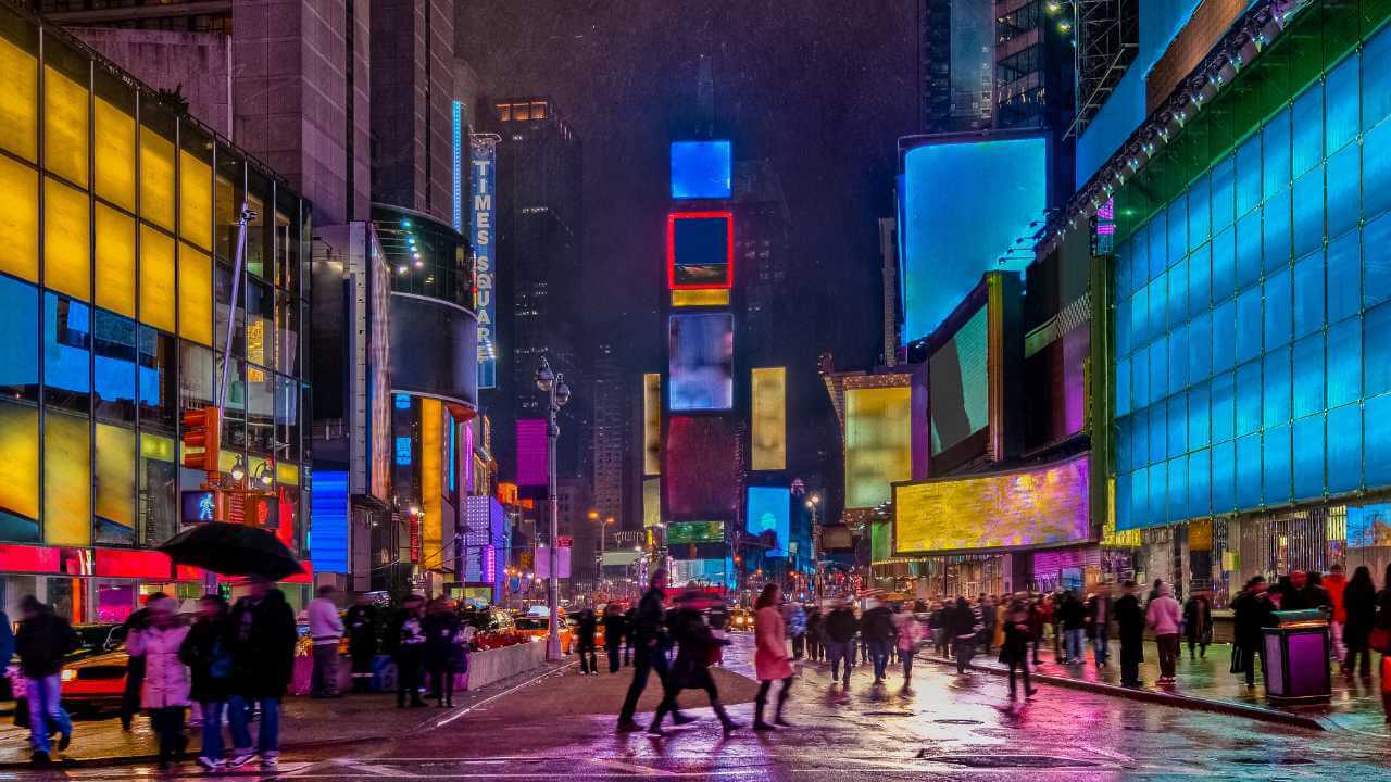 times square in new york city at night with people walking and holding umbrellas