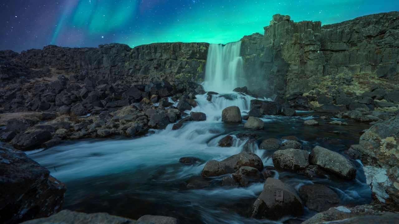 view of northern lights from the bottom of a waterfall 