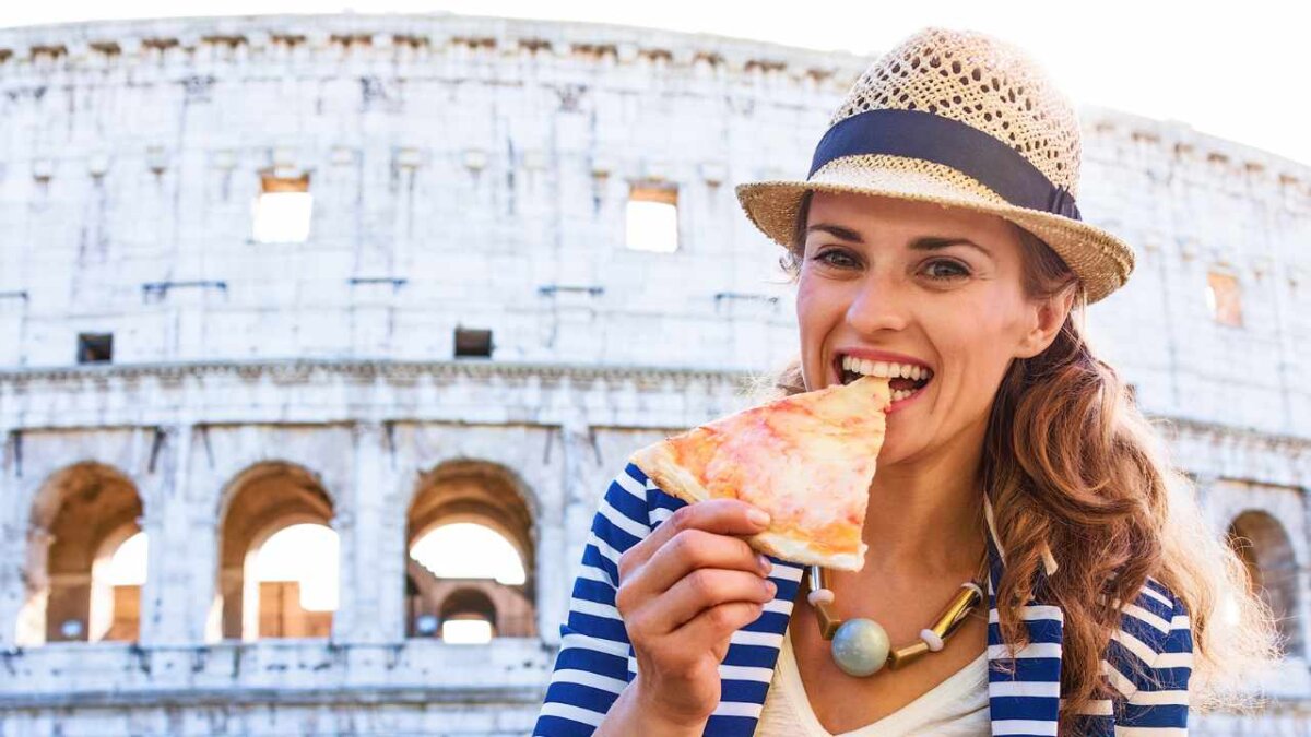 woman eating pizza in front of colosseum in rome