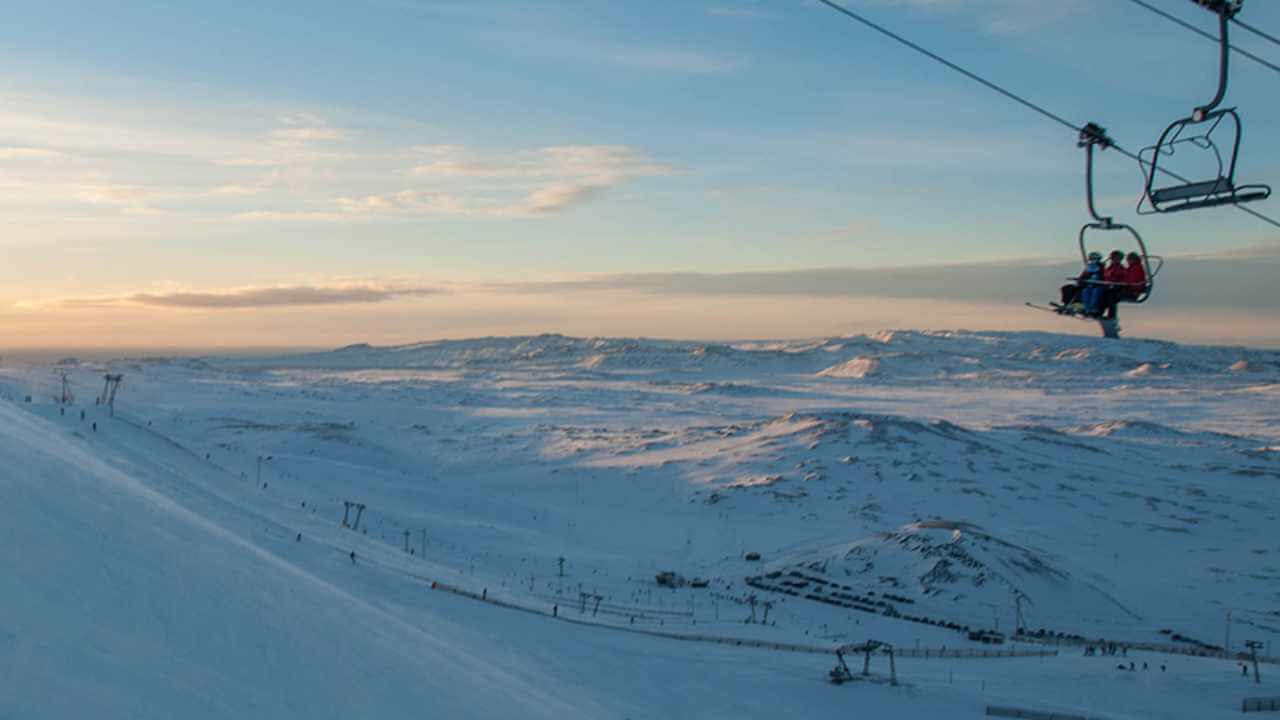 two people on a ski lift above mountains in iceland