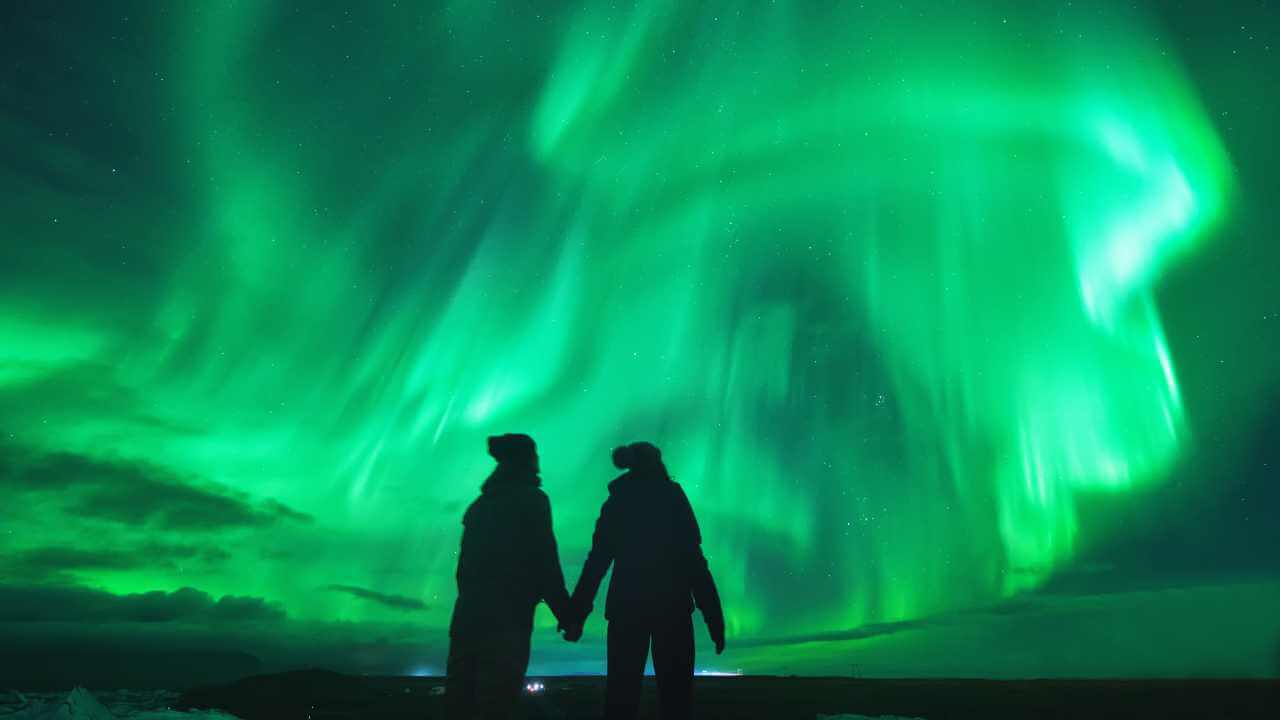 two people admiring the greenish blue northern lights in iceland