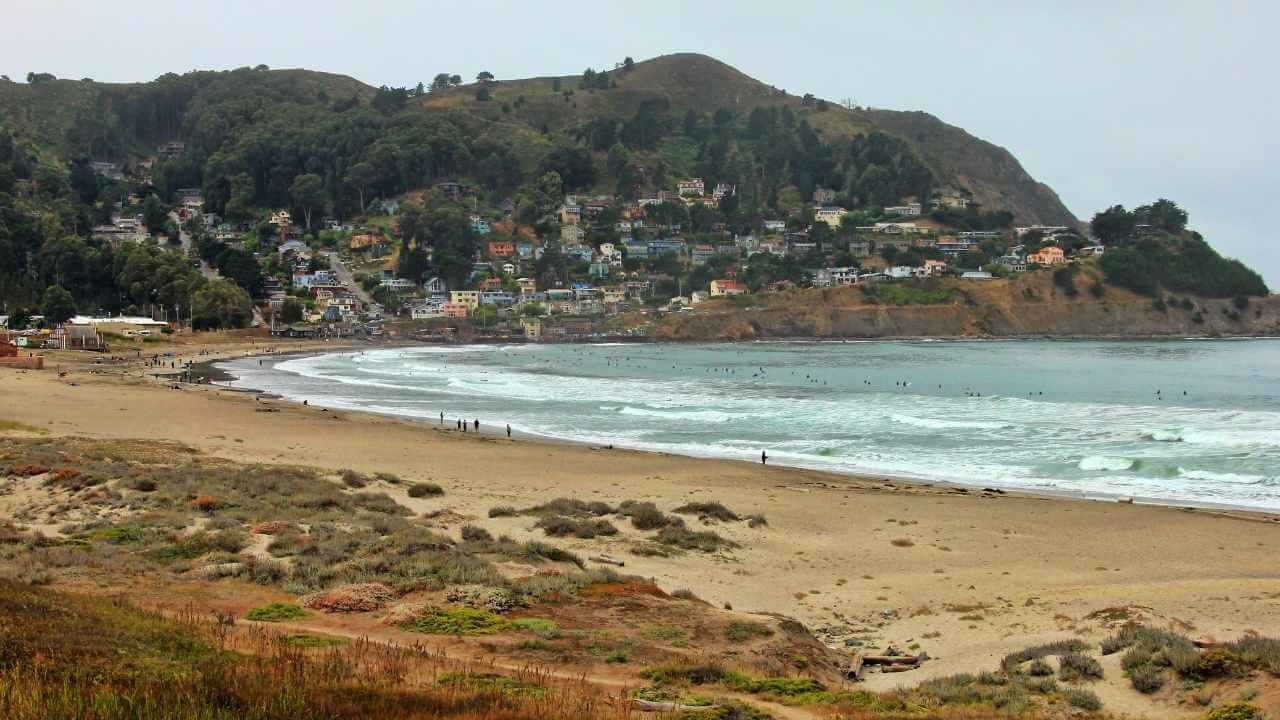 a view of a beach with houses and hills in the background