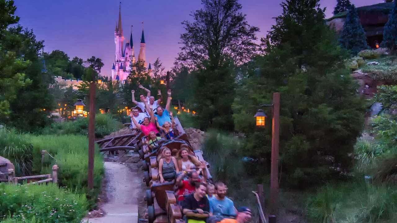 people on seven dwarfs mine train at night, cinderella castle in background at sunset