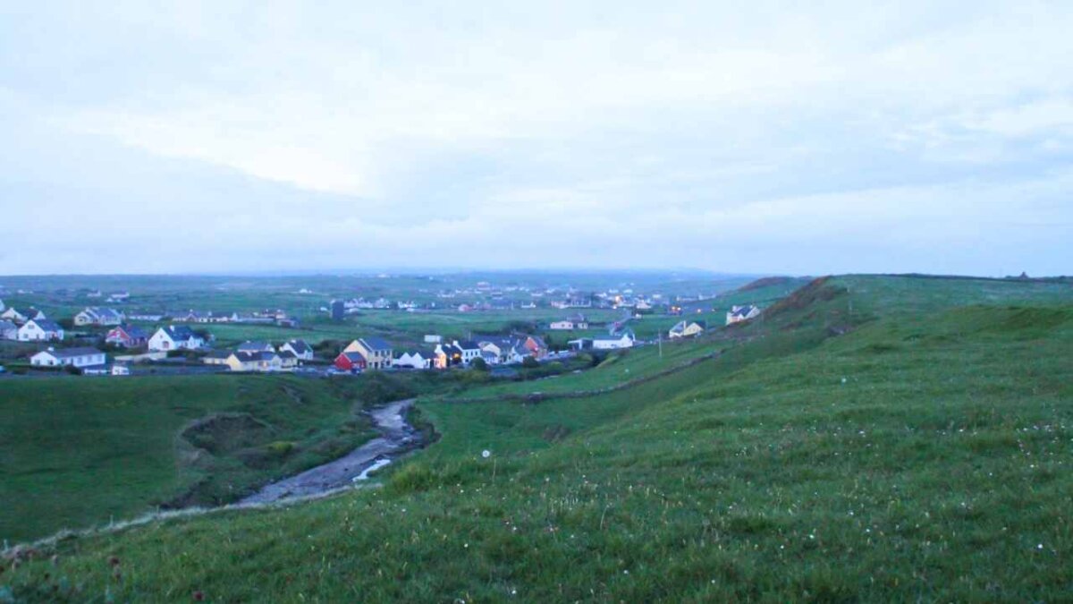 a grassy hillside with houses in the distance