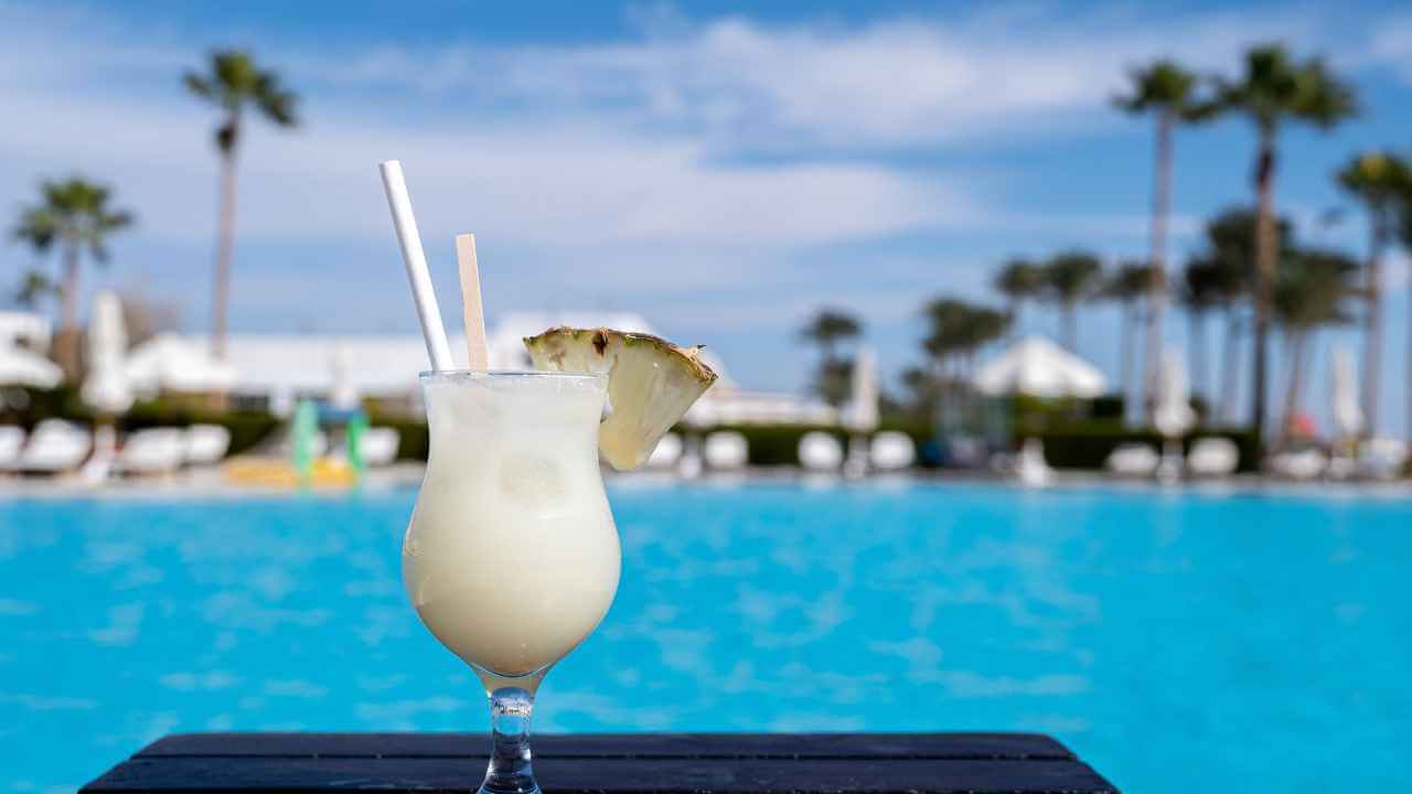 pina colada cocktail on wooden table in front of pool