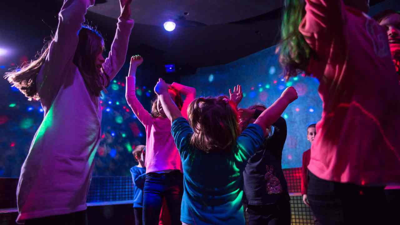 a group of children dancing in front of colorful lights
