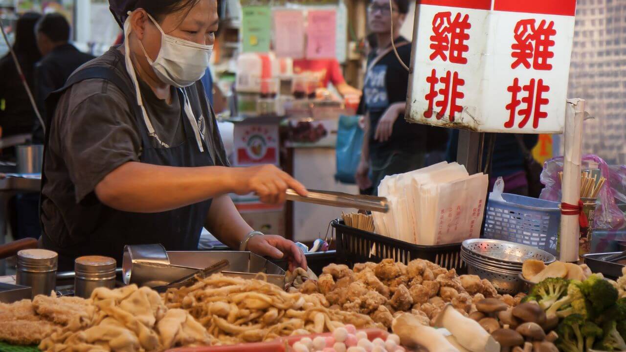 a person wearing a face mask is preparing food at an asian market