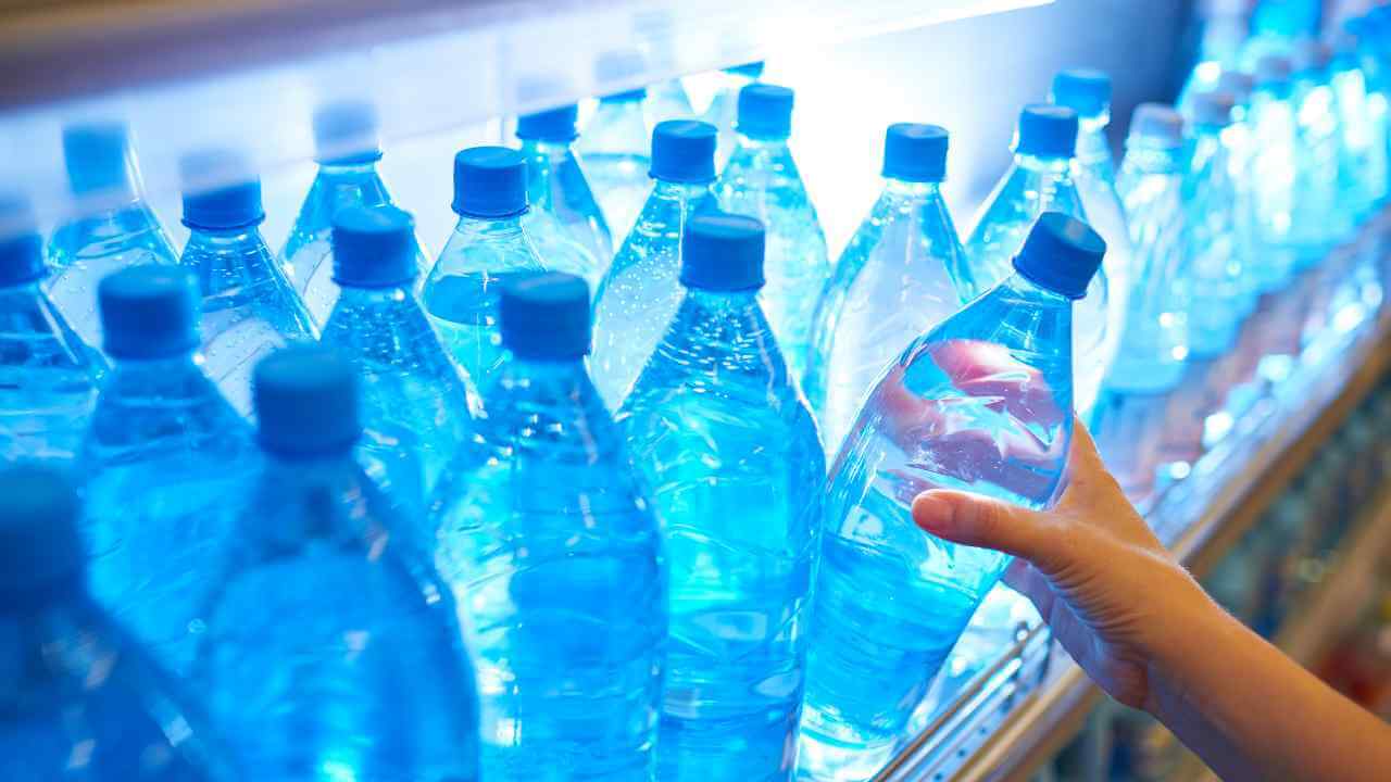 a person holding a bottle of water in front of a shelf full of blue bottles