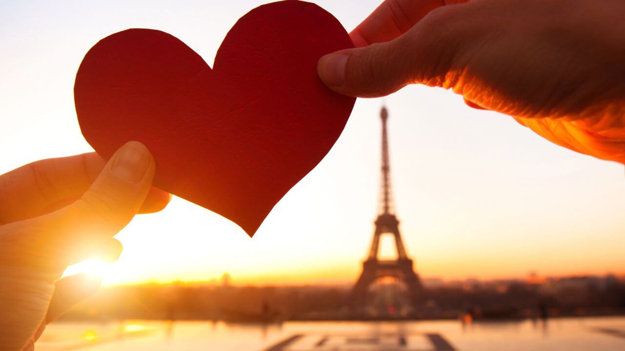 two people holding up a red heart in front of the eiffel tower