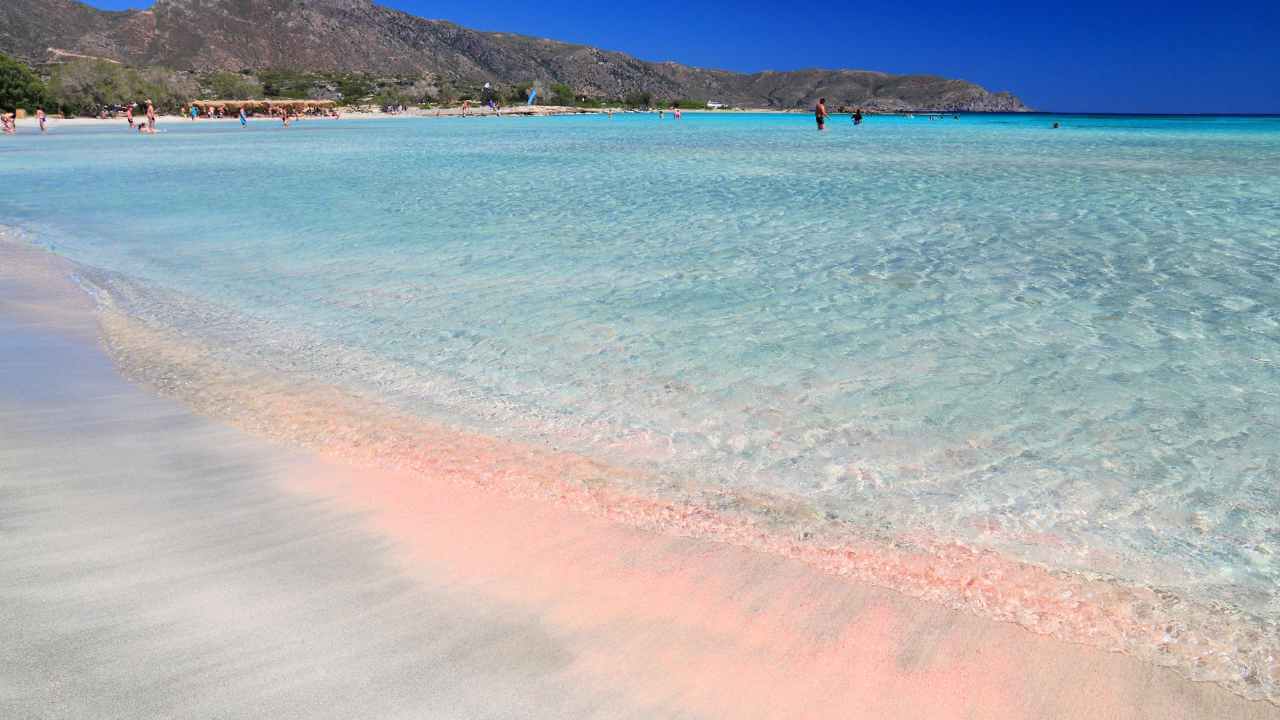 a sandy beach with pink water and mountains in the background