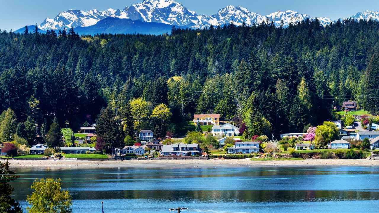 a small town sits on the shore of a lake with snow capped mountains in the background
