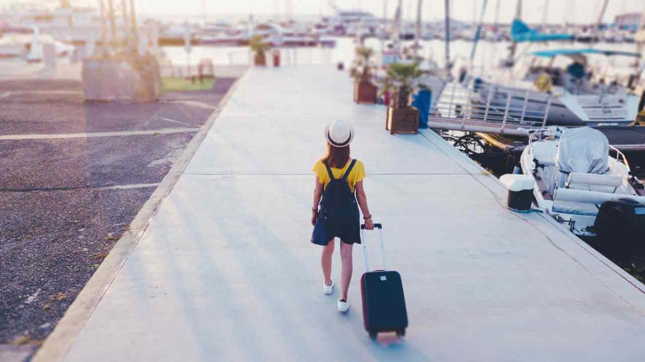 a person with a suitcase walking on a dock with boats in the background