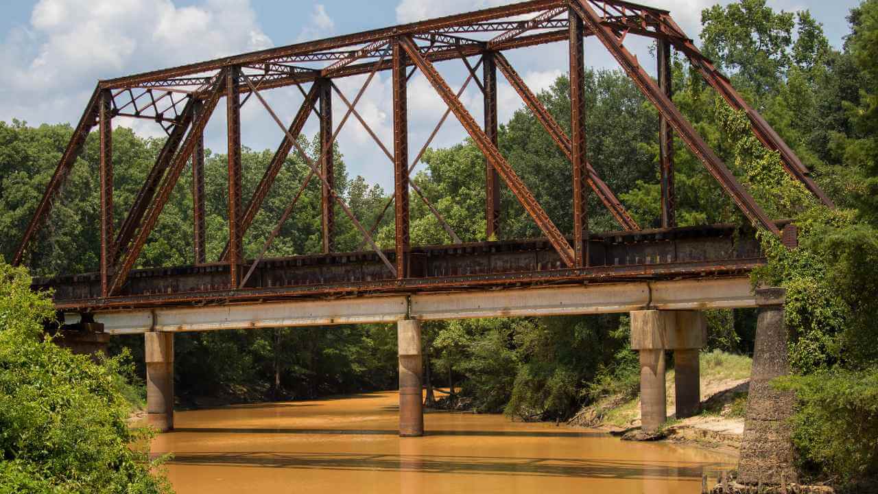 a rusty old train bridge over a muddy river