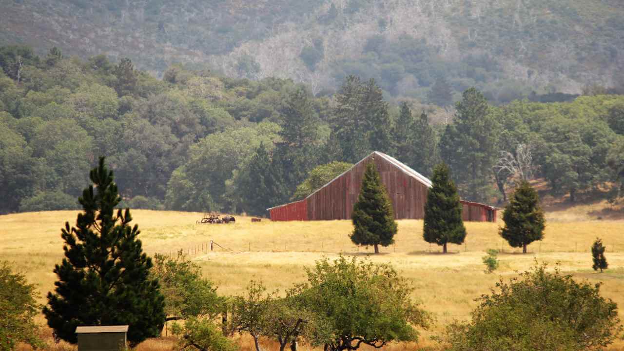 an old red barn sits in the middle of a field