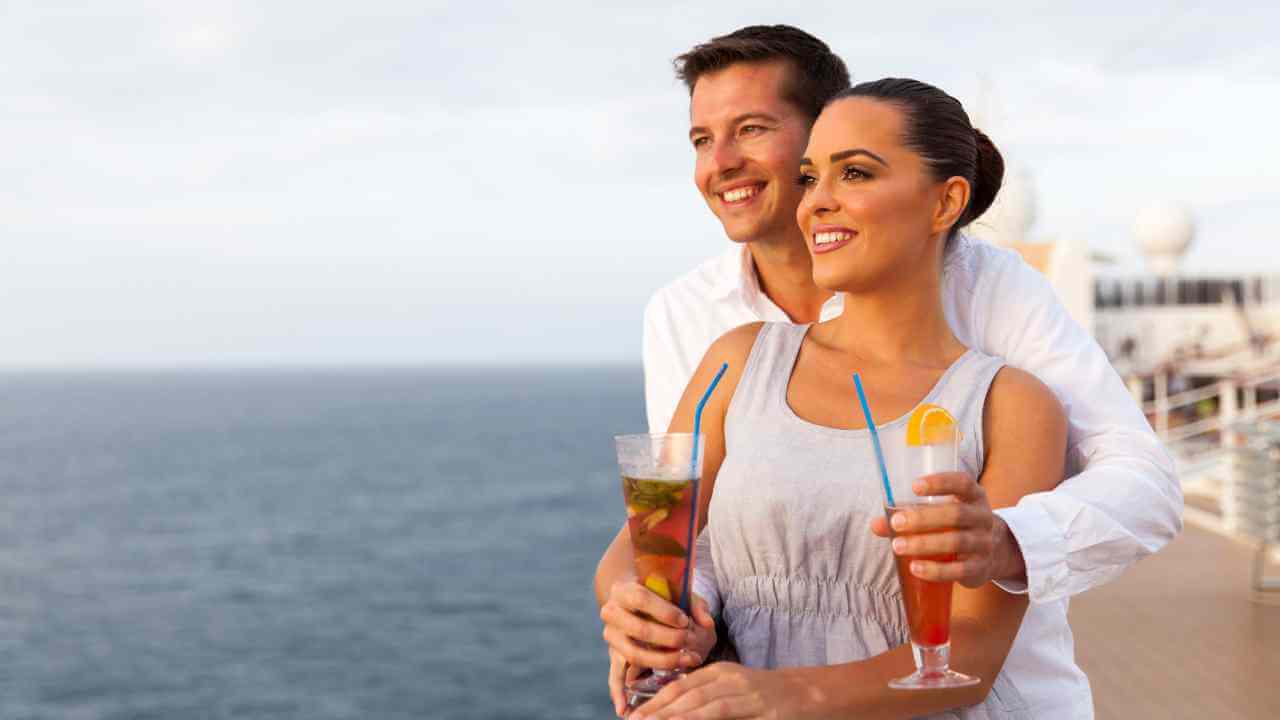 Two people holding drinks on the deck of a cruise ship