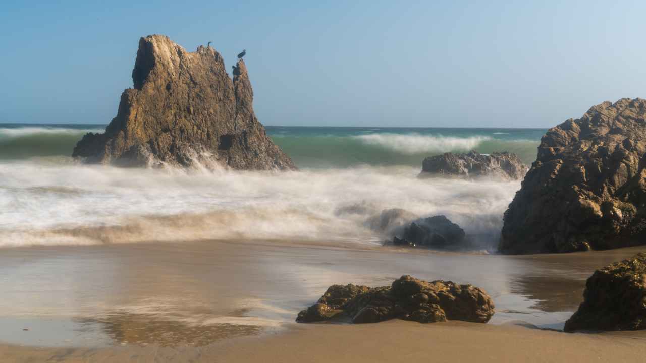 a rock formation on the beach with waves crashing against it