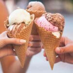 three people holding ice cream cones in front of each other
