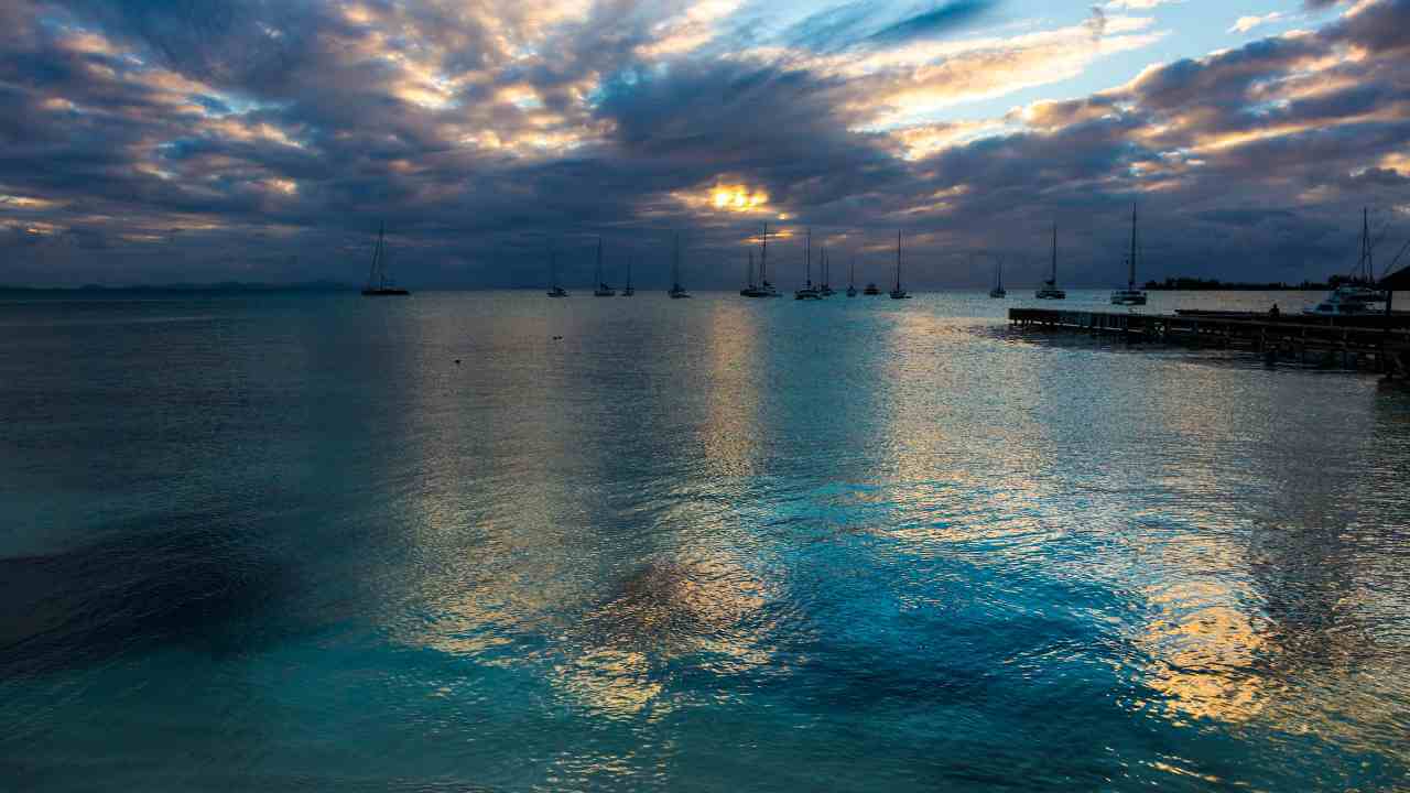 sailboats are docked in the water under a cloudy sky