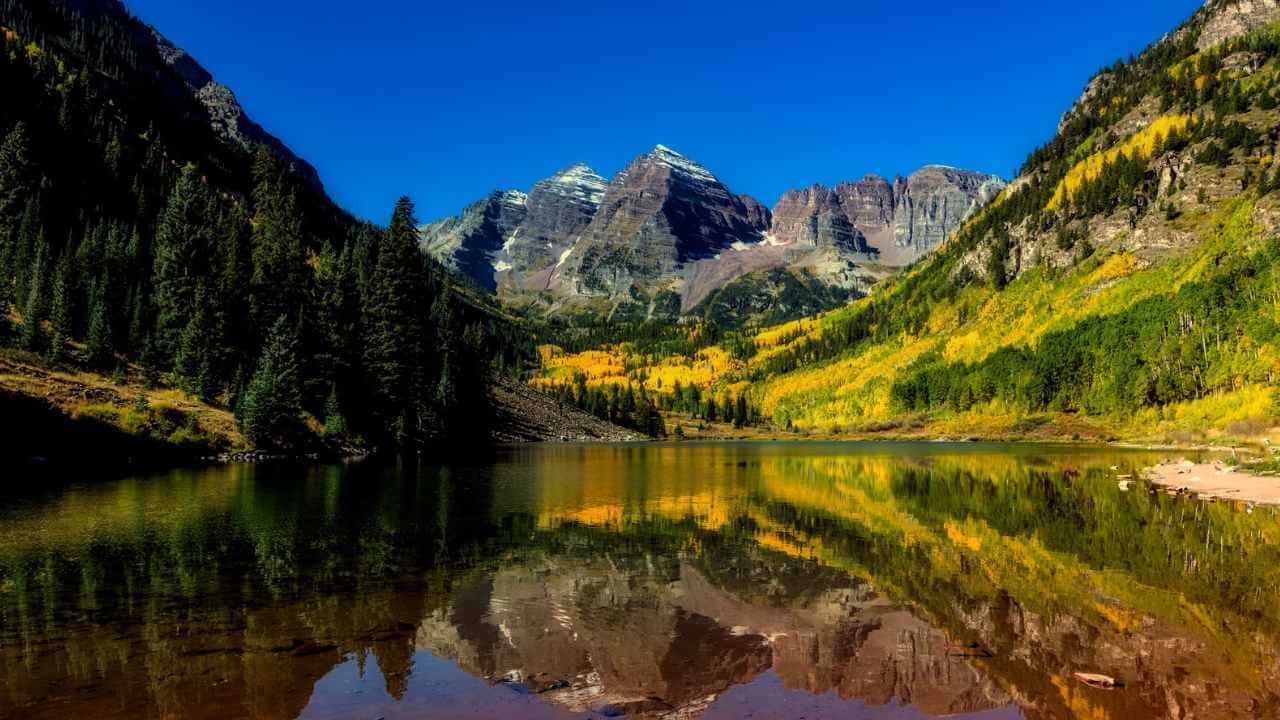 the maroon bells mountain range is reflected in the water