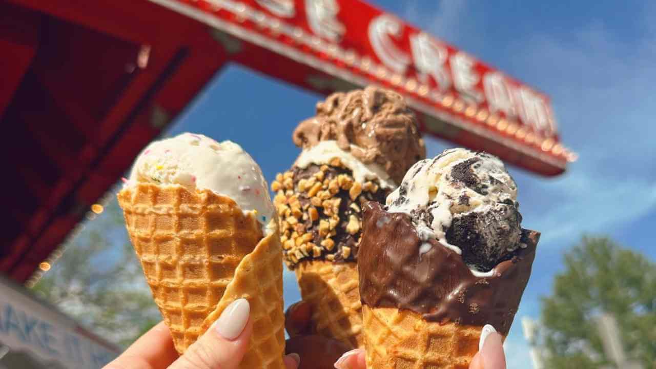 three ice cream cones being held in front of ice cream sign 