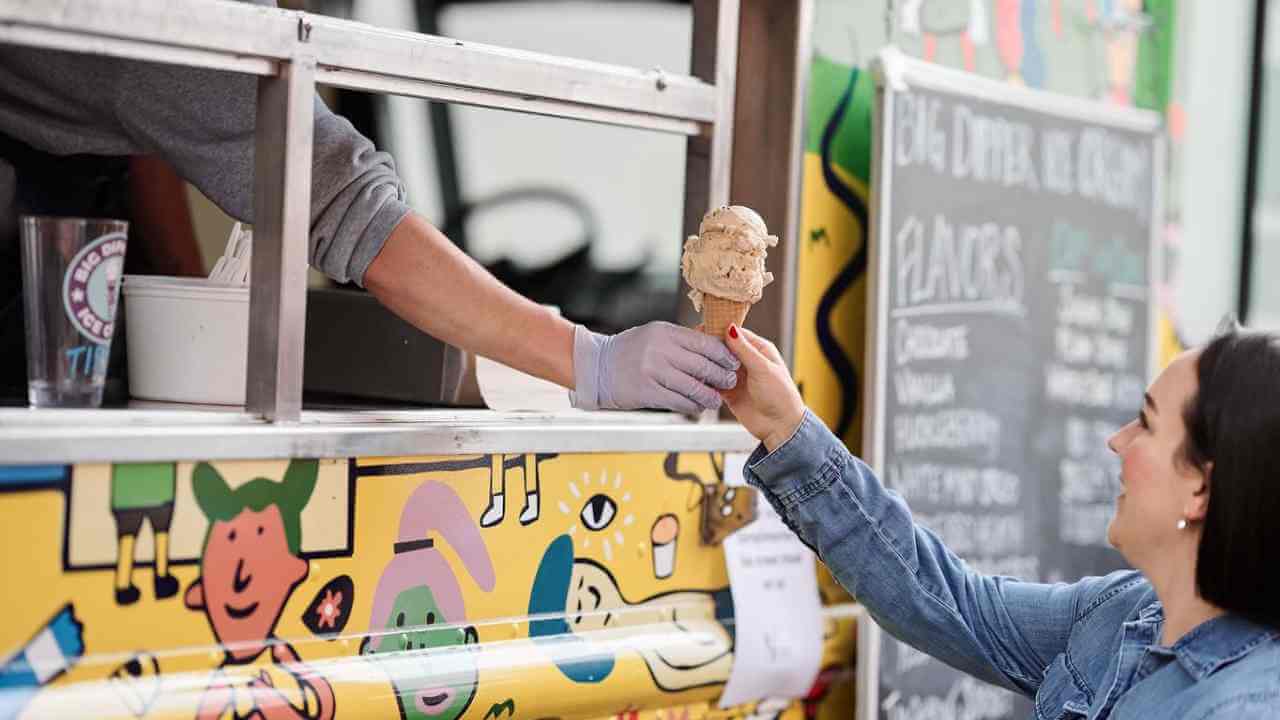 a person handing an ice cream cone to another person at a food truck