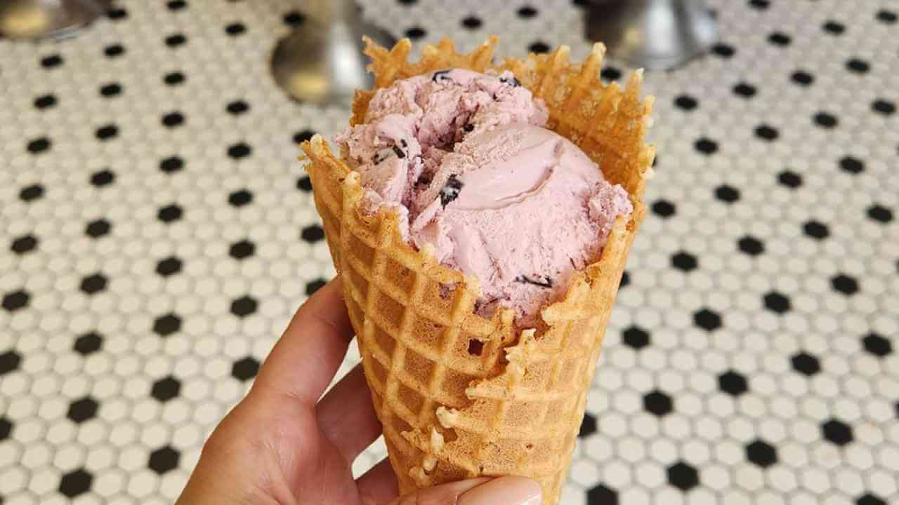 a hand holding a waffle cone with a scoop of ice cream