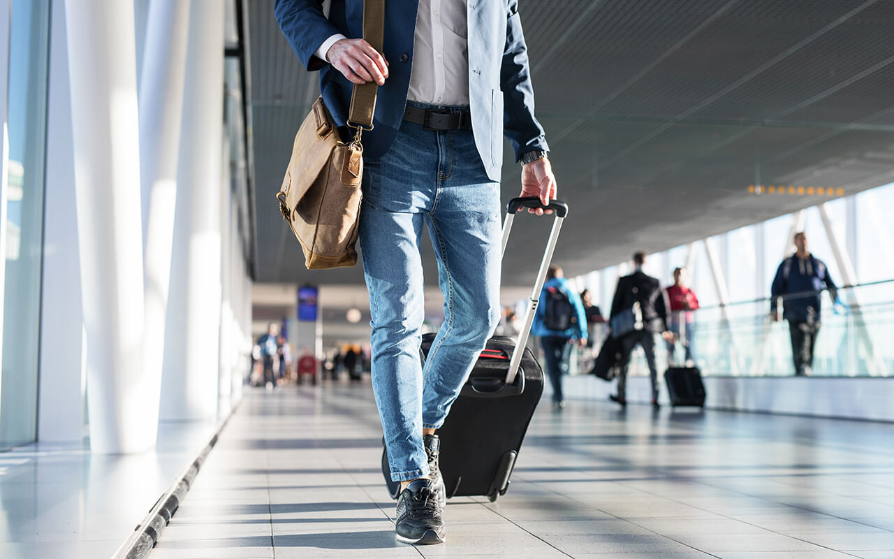 Man with shoulder bag and hand luggage walking in airport terminal